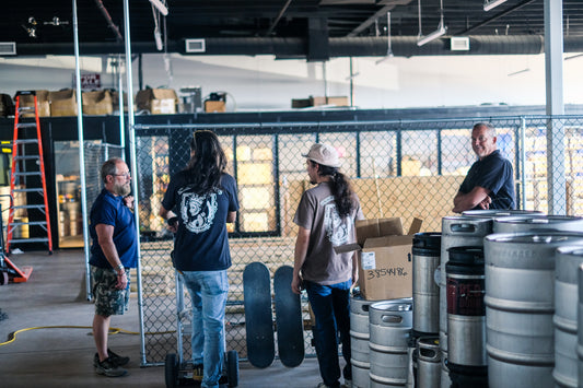 Team members at Unhinged Brewing discussing plans inside the unfinished distillery space, surrounded by kegs and equipment, highlighting the behind-the-scenes of their expansion and innovation in Albuquerque.